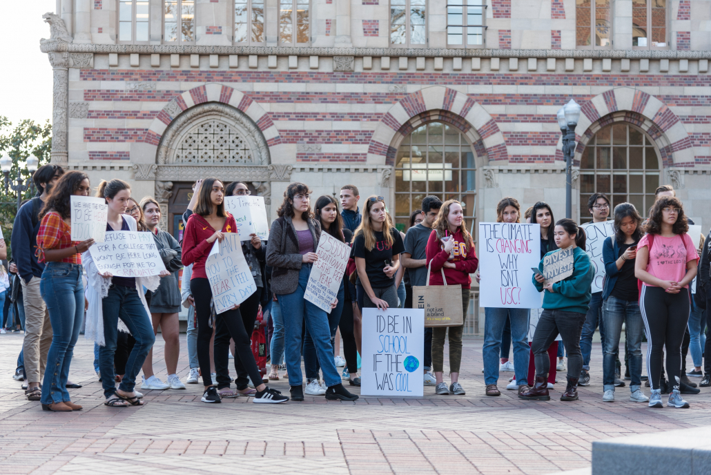 A group of students stand in front of the red brick building of student union holding banners