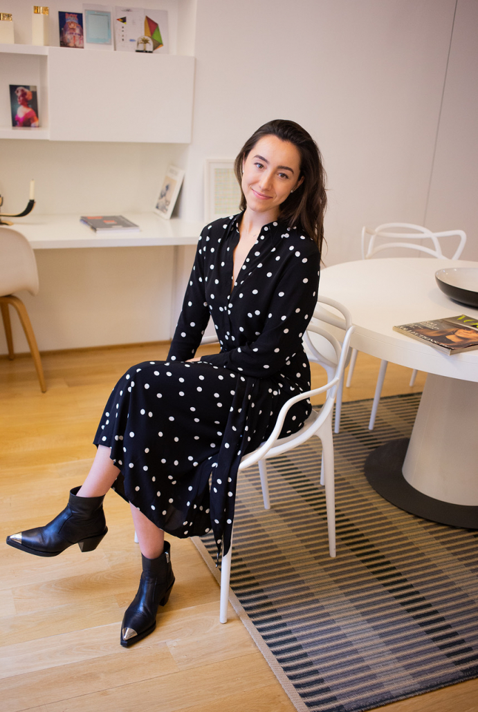 Carlota Rodriguez-Benito sitting on a white chair wearing a black dress with white polka dots. 