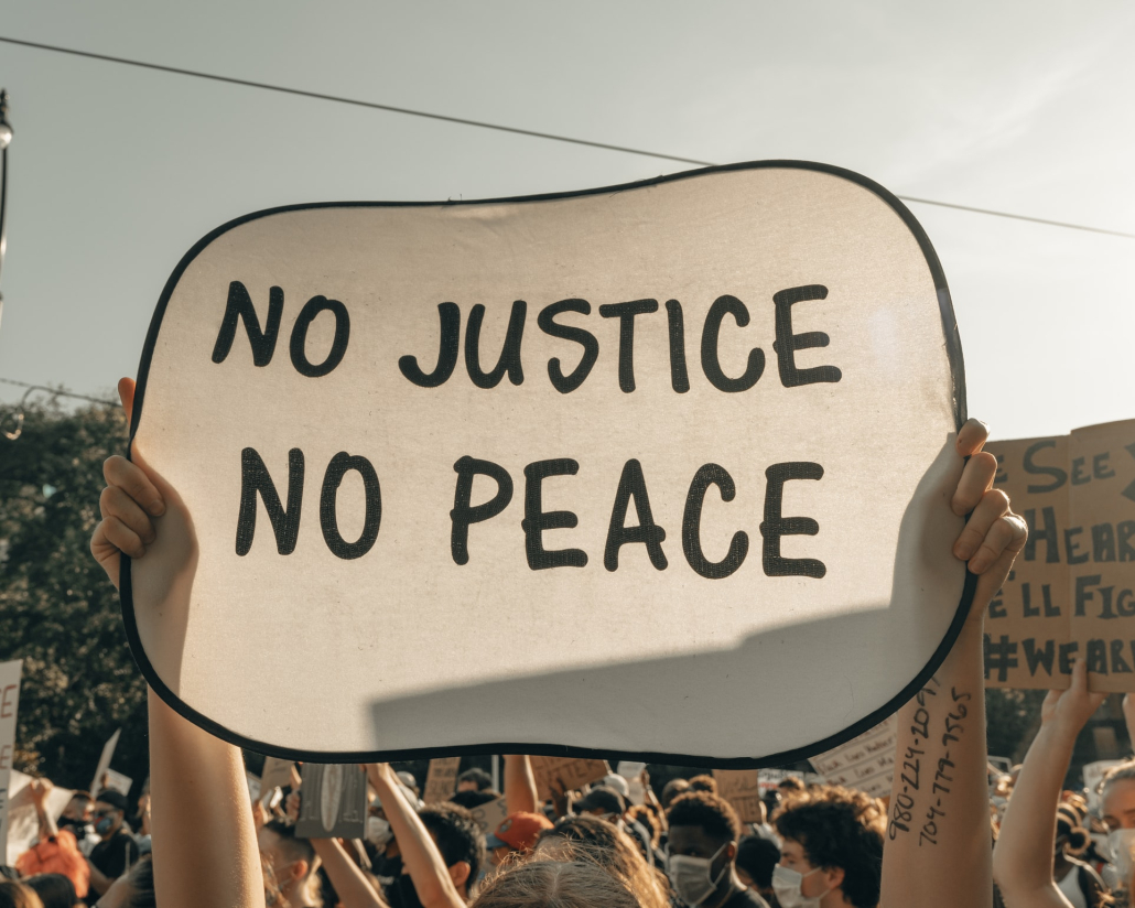 Photo of a civil rights/social movement with a person holding up a sign that says "No justice no peace."