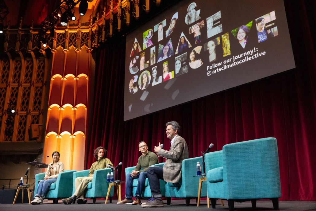 Four speakers sit on teal couches on the Bovard stage. There is an Arts & Climate Collective design on the big screen projected behind them. 