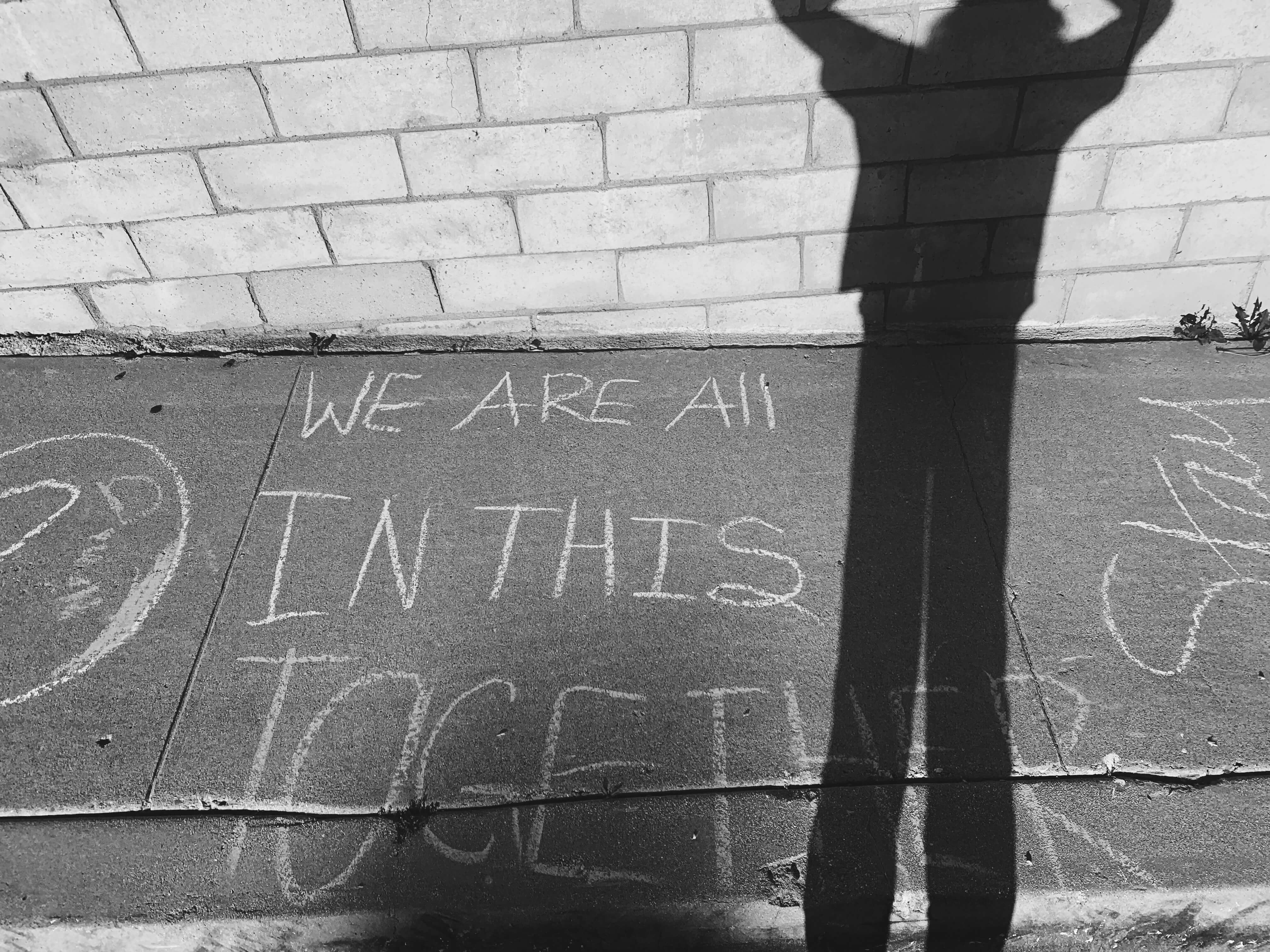 Chalk on street ground that says 'WE ARE ALL IN THIS TOGETHER'