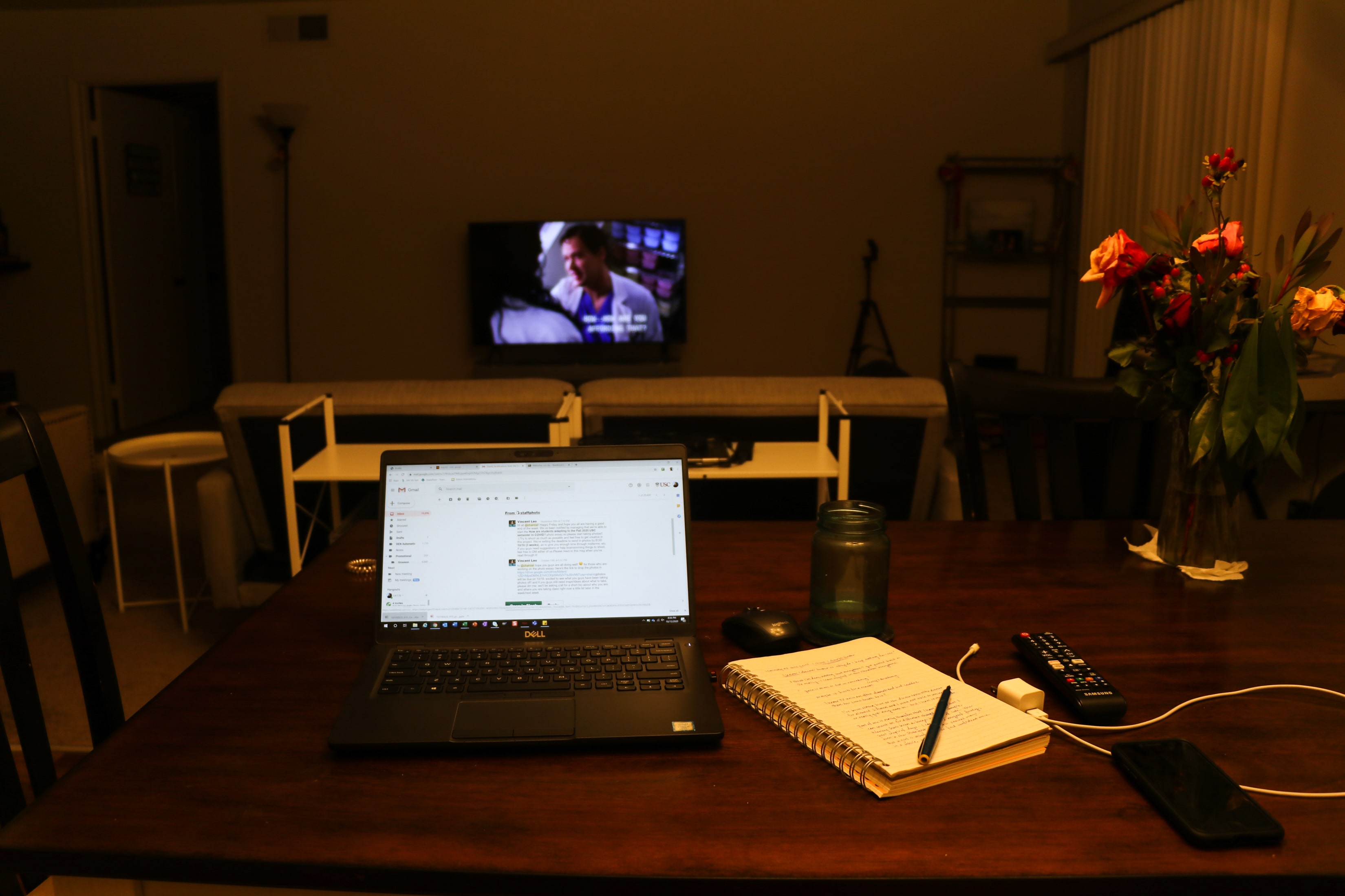 Laptop and notebook on empty table before a TV