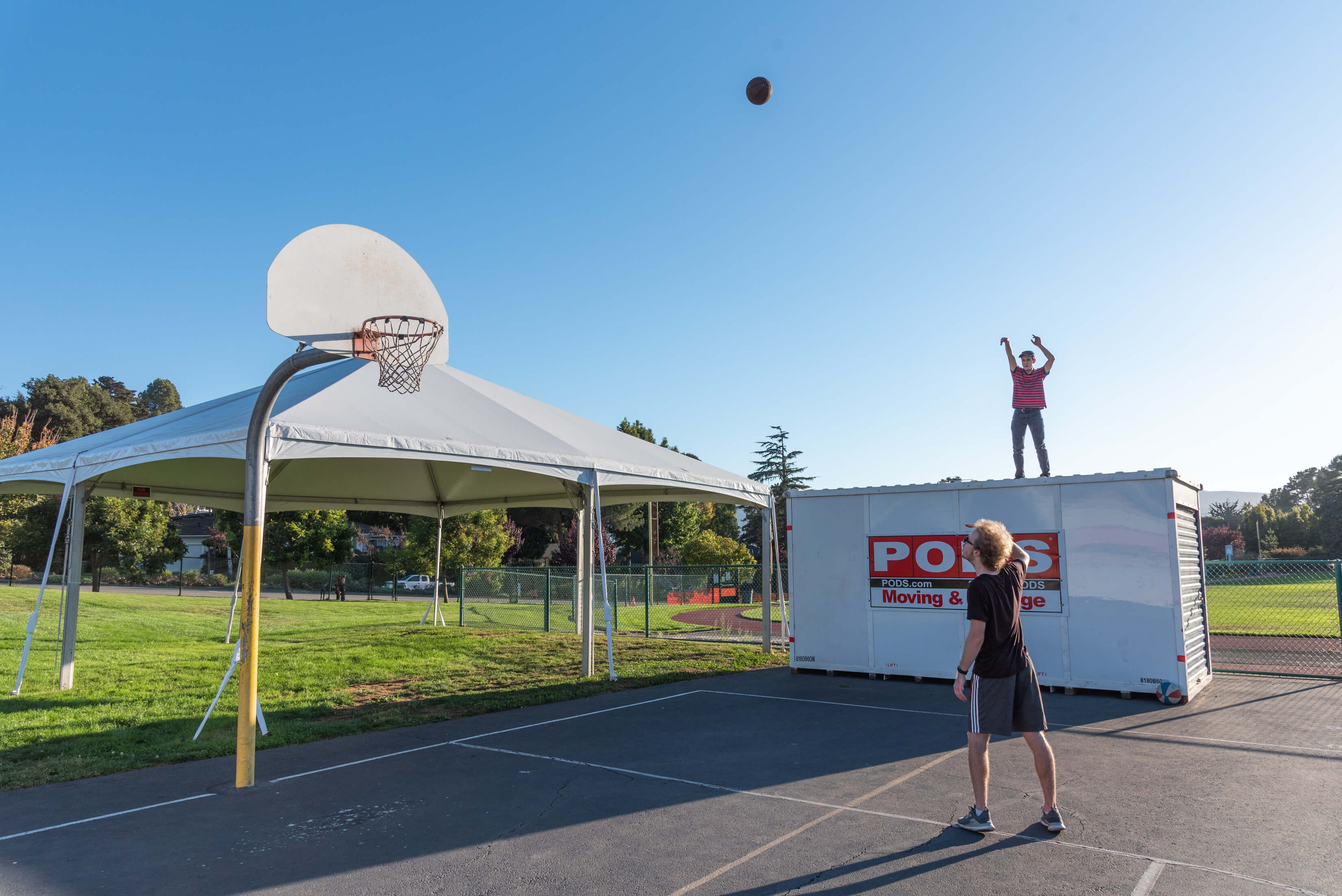 Person shooting basketball into hoop and another person looking