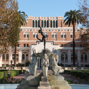 This is a photo of the fountain at the center of Alumni Park at USC. In the background is Doheny Memorial Library, partially in the shade on a bright sunny day.