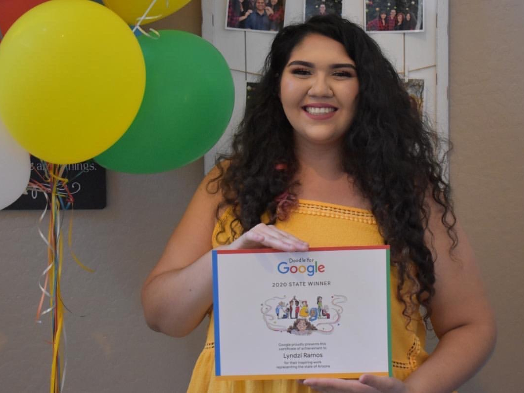 Ramos smiles in front of a balloon bouquet Google gifted her and holds her winning drawing. 