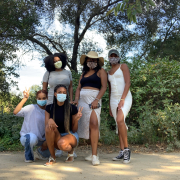A group of five girls in front of trees with masks on. Three of them are standing at the back with two of them kneeling.