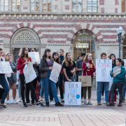 A group of students stand in front of the red brick building of student union holding banners