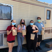 Four people standing with brown paper bags wearing masks