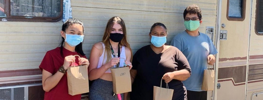 Four people standing with brown paper bags wearing masks