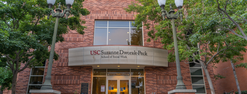 The red brick building of the Suzanne Dworack-Peck school of social work with trees on both sides.