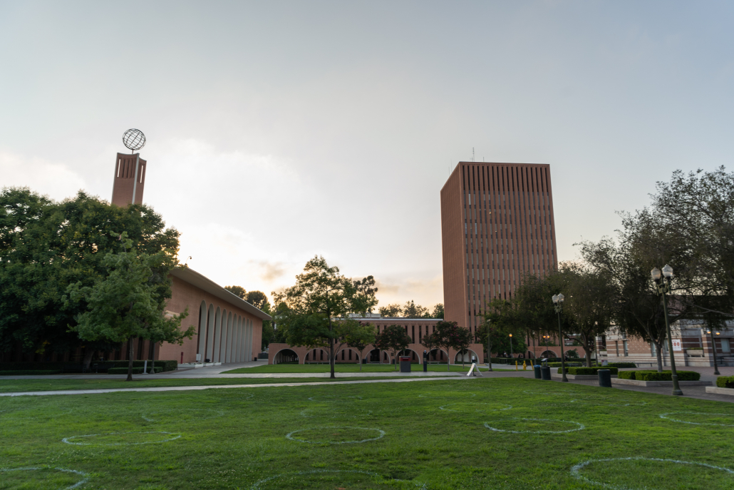 A green grass lawn is shown in front of two red brick buildings, including the Social Sciences Building which has a metal globe on top of a tower.