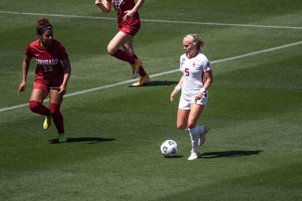 Penelope Hocking, number five, kicks the ball down the field as a defender approaches.