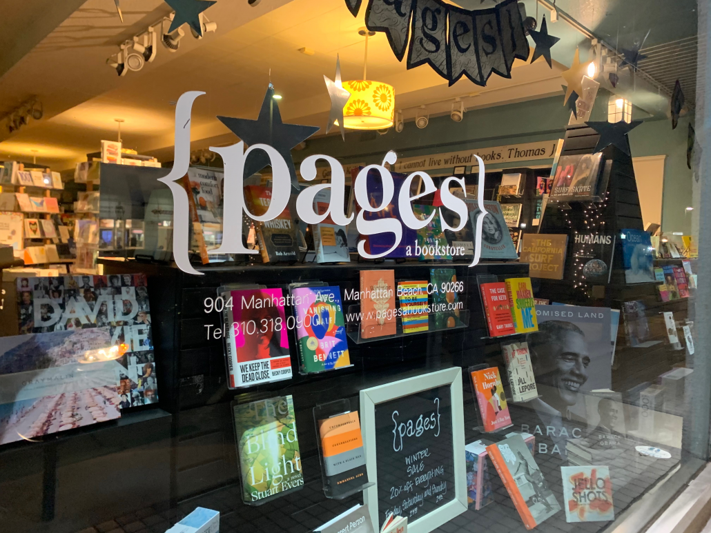 A photo of the outside window of the Pages bookstore; in front there is a display of the latest published works on display.
