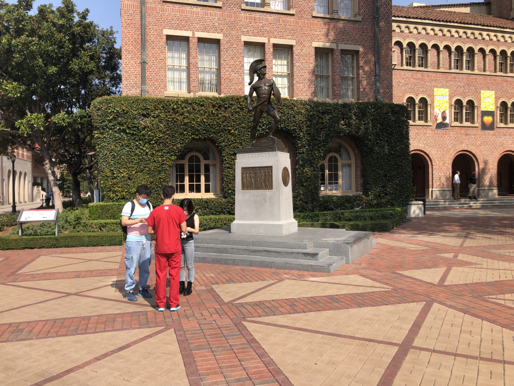 Two people hand out fliers to a passerby in front of Tommy Trojan.