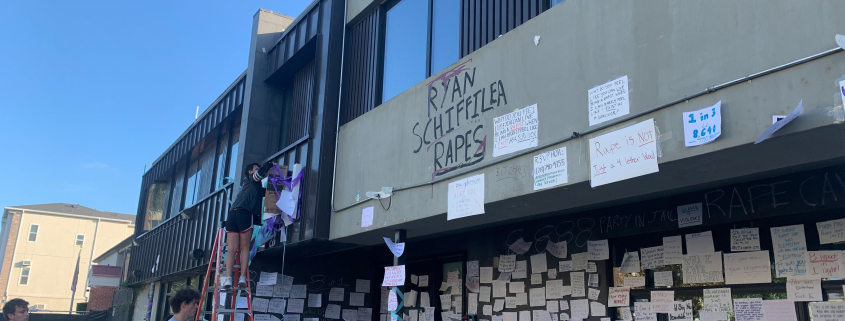 Image of Sigma Nu house with papers taped to the wall and spray paint that reads “Ryan Schiffilea rapes.”