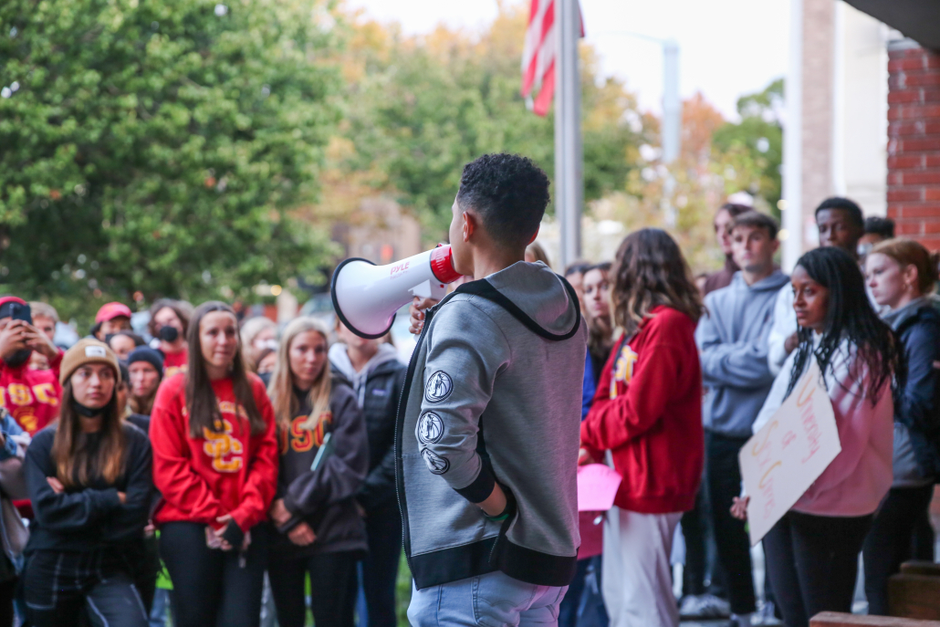 A student speaks into a megaphone in front of a crowd of people.