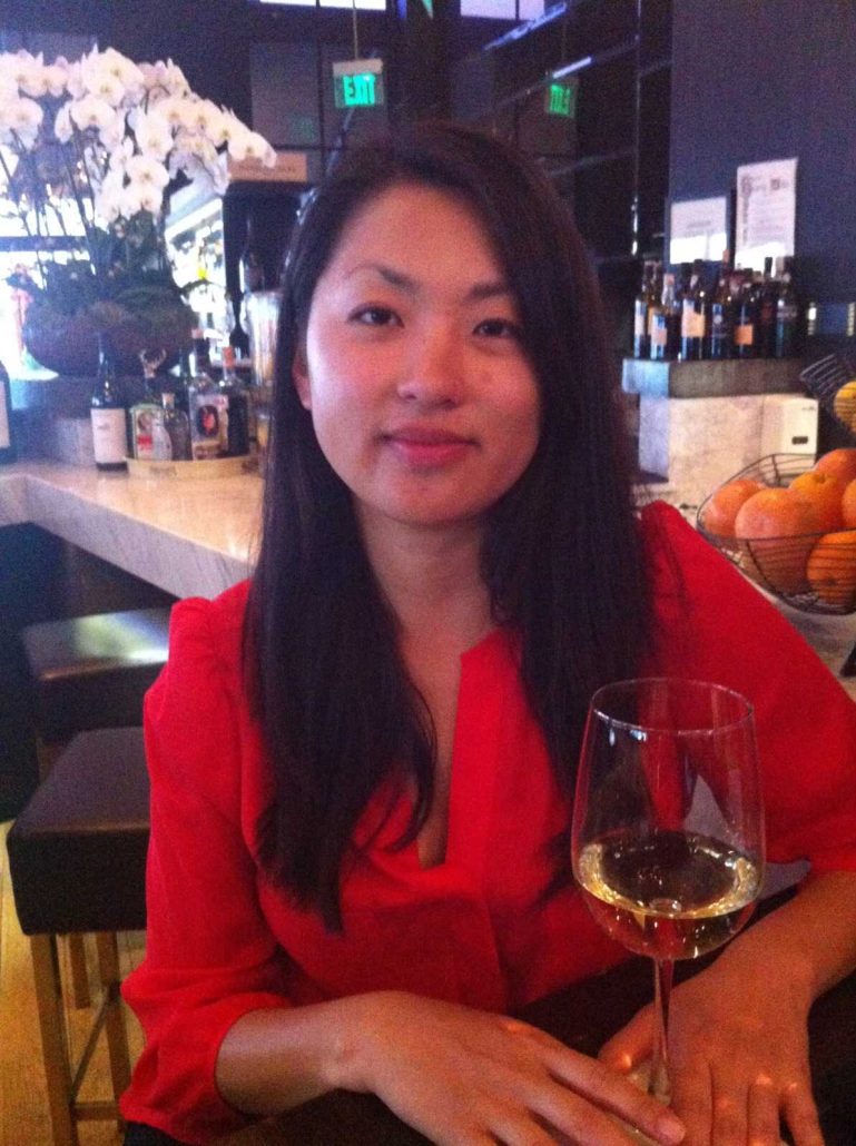 Sara Yim sits wearing a red top at a restaurant with a glass in front of her. 