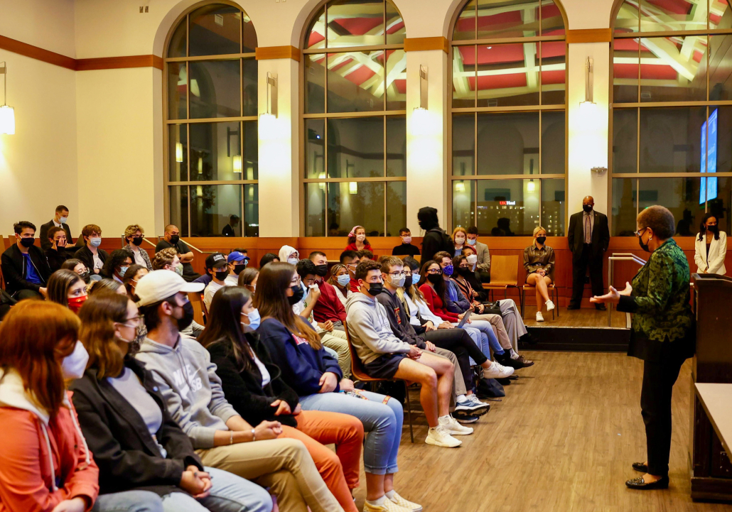 Students sit in rows in the Ronald Tutor Campus Center. Karen Bass stands at the front of the room. 