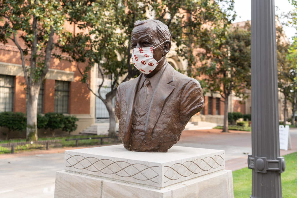 Photo of bust statue on campus with a USC mask on its face. 