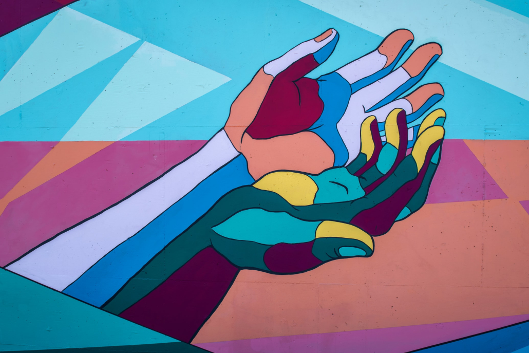Photo of a mural of two hands, palms open, with a variety of bright colorful paints.