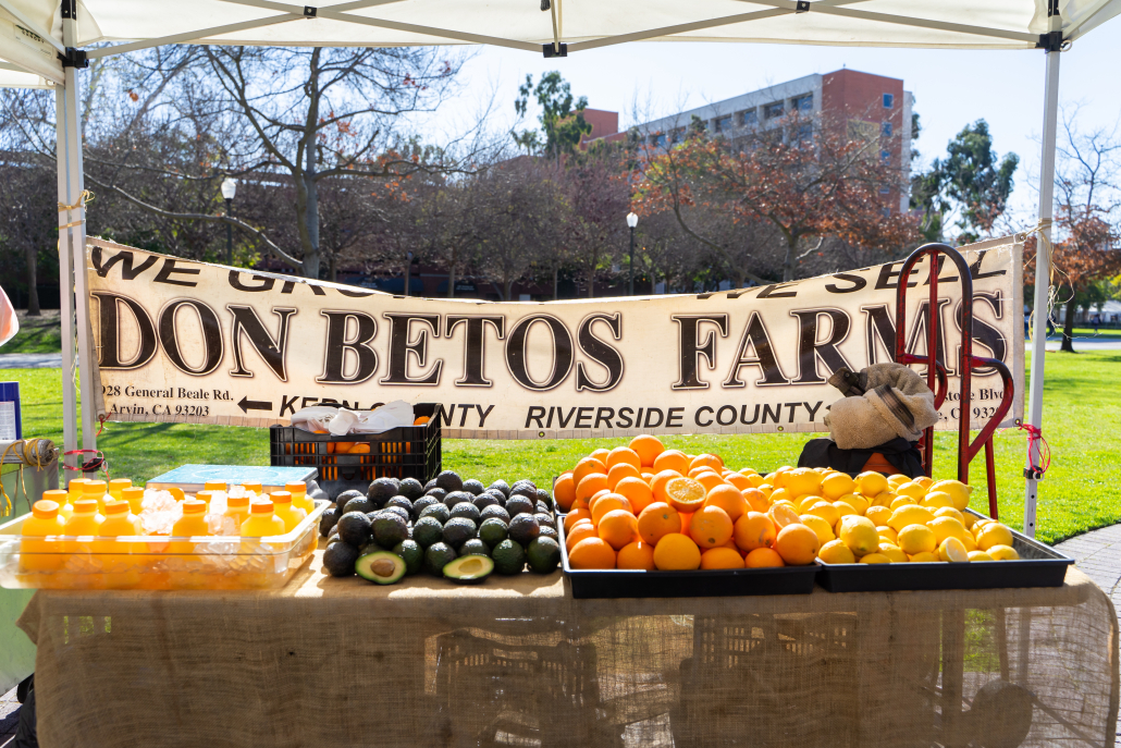 Photo of oranges, avocados, lemons and orange juice on a farmers market stand with a banner that says "Dan Betos Farms"