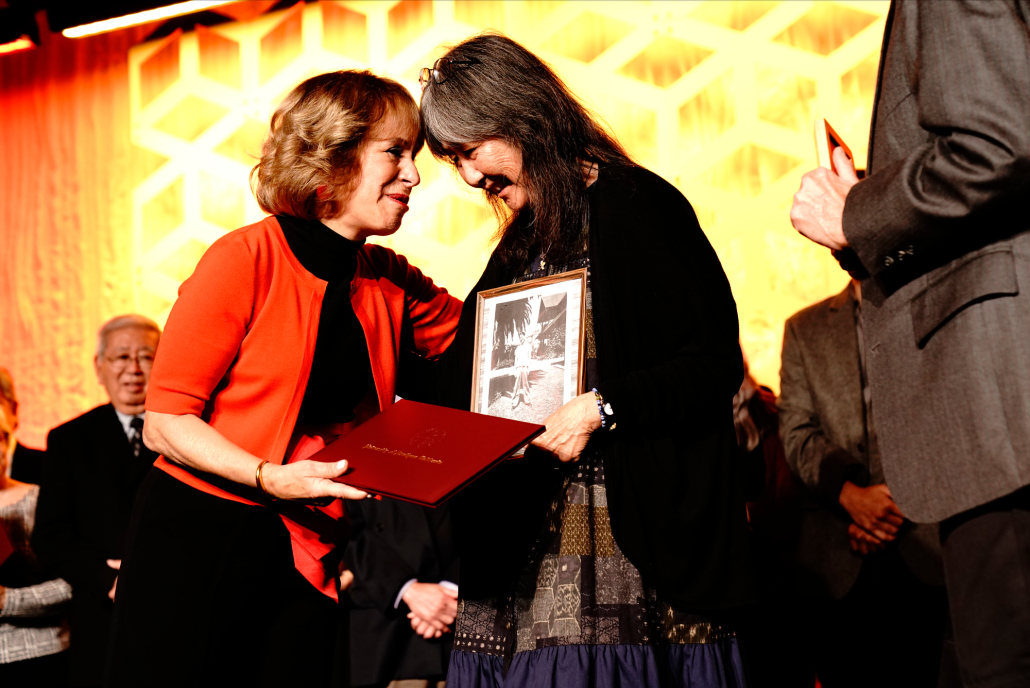 Carolyn Sugiyama Classen (center), carrying a photograph of her late father and WWII-era University of Southern California dental student Francis Sueo Sugiyama, accepts a posthumous honorary degree in his honor from Dr. Carol L. Folt (left), president of the University of Southern California, at a USC Asian Pacific Alumni Association gala at the Langham Huntington hotel in Pasadena, California, U.S., April 1, 2022. Nisei (‘second generation’) Japanese-American students at USC were forcibly sent to internment camps after the 1941 bombings, and had their college careers undermined when USC refused to release their transcripts for those who sought to transfer to other schools. 