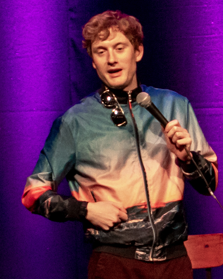 Photo of James Acaster performing stand-up comedy.
