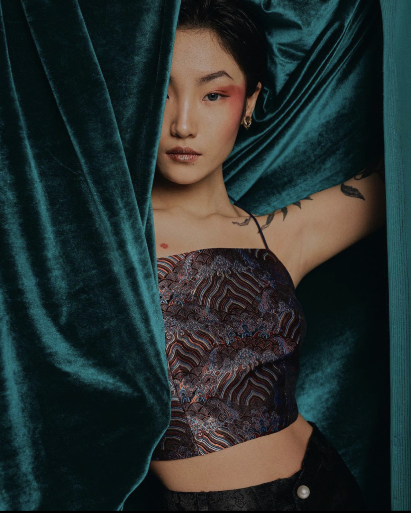 A model in a DAWANG top poses in a green velvet curtain.