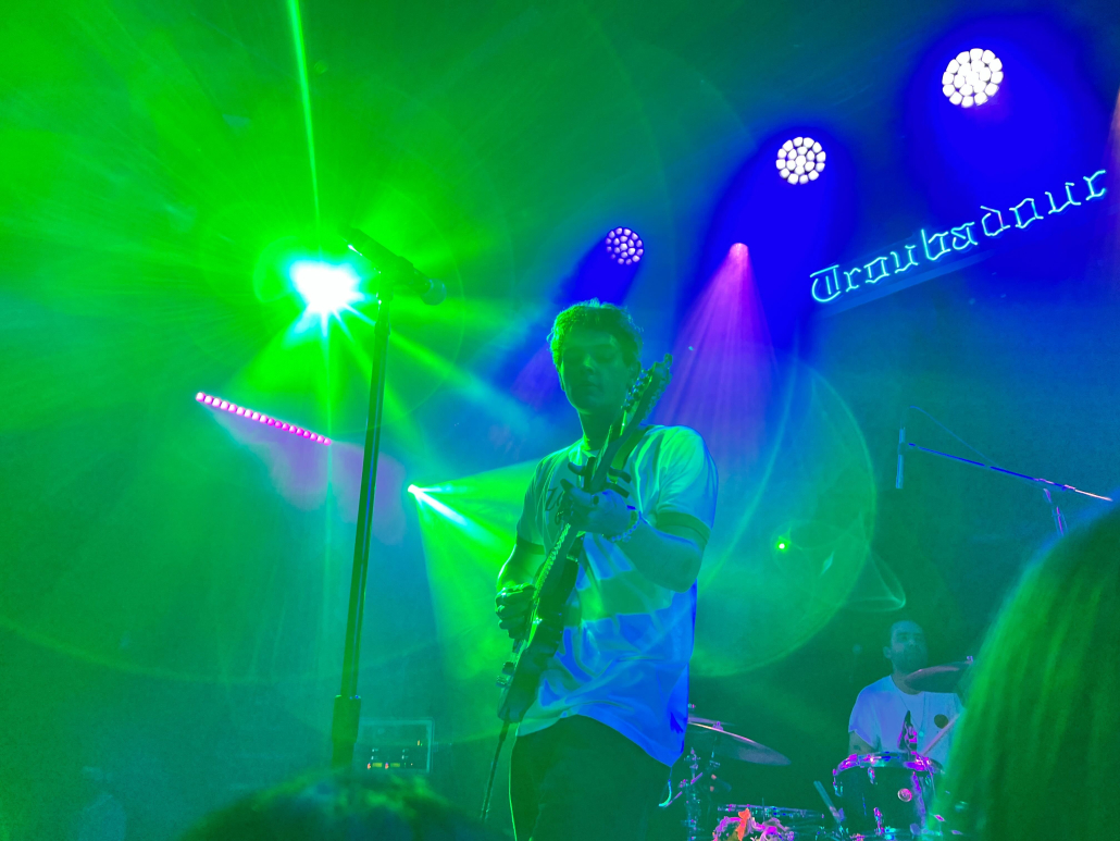 Thomas Headon performing at the Troubadour with guitar in green lighting. 