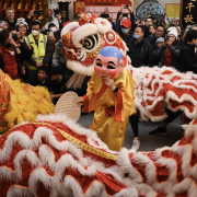 A figure dress like a monk dances while a dragon dance is performed around them.