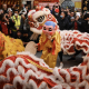 A figure dress like a monk dances while a dragon dance is performed around them.