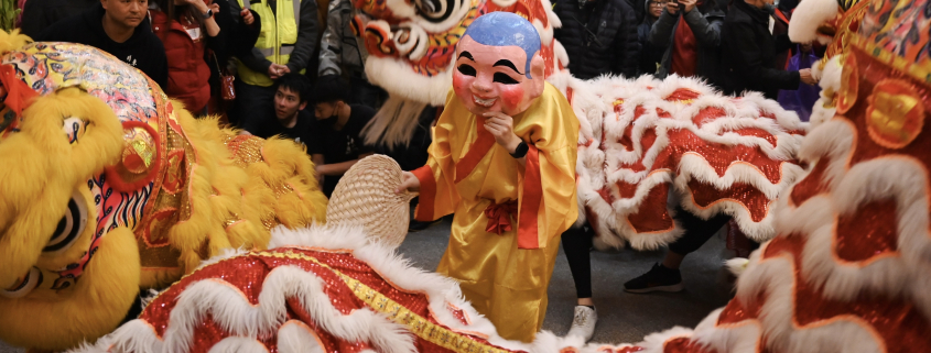 A figure dress like a monk dances while a dragon dance is performed around them.