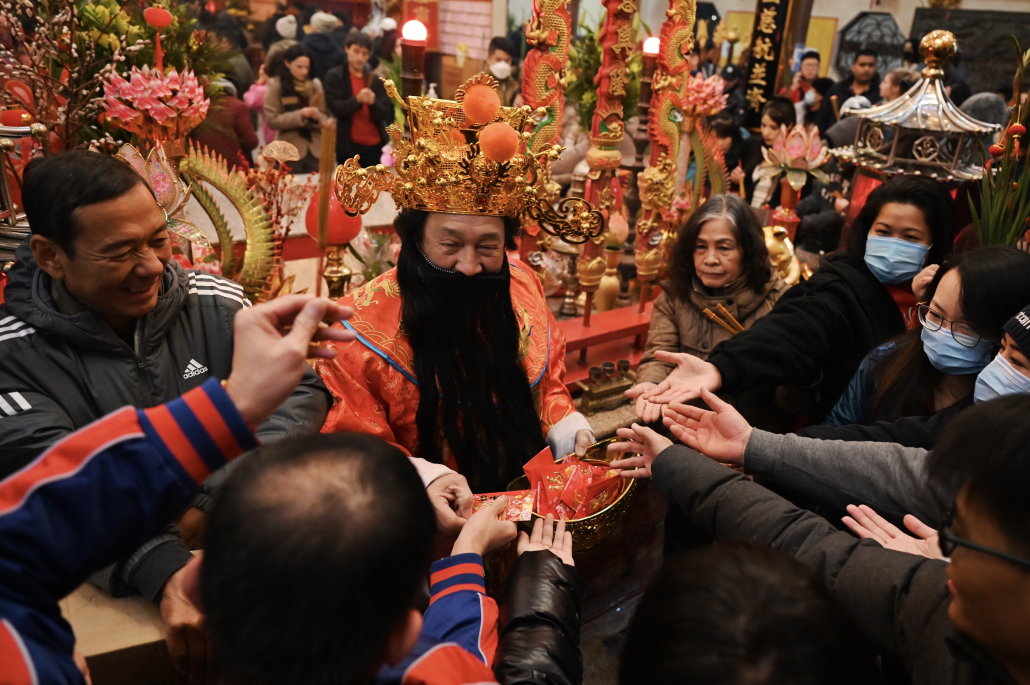 A man in royal garb hands out red envelopes to a crowd.