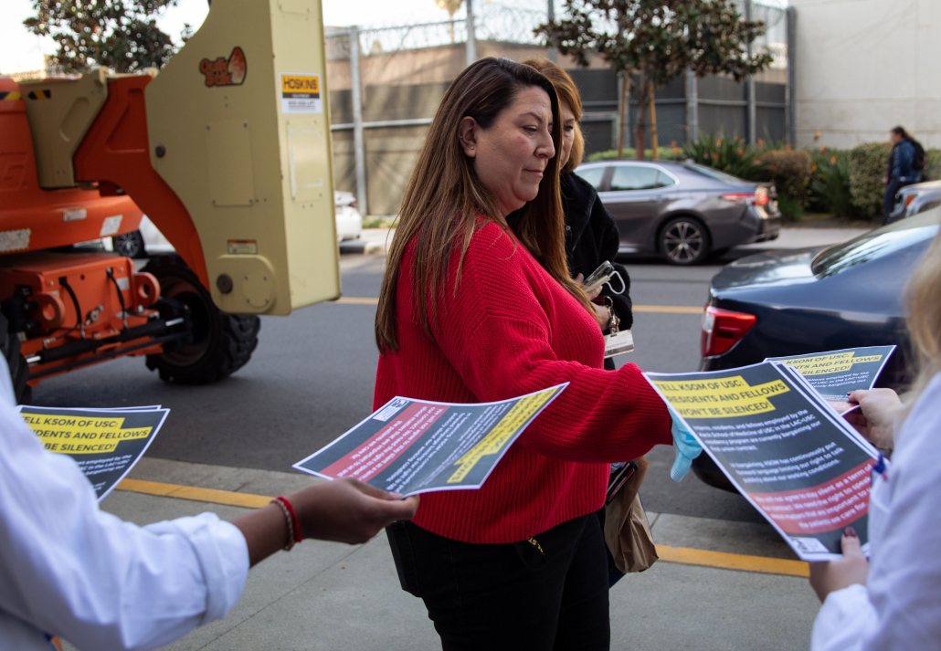 A woman in a red sweatshirt hands out fliers in support of Keck School of Medicine residents.