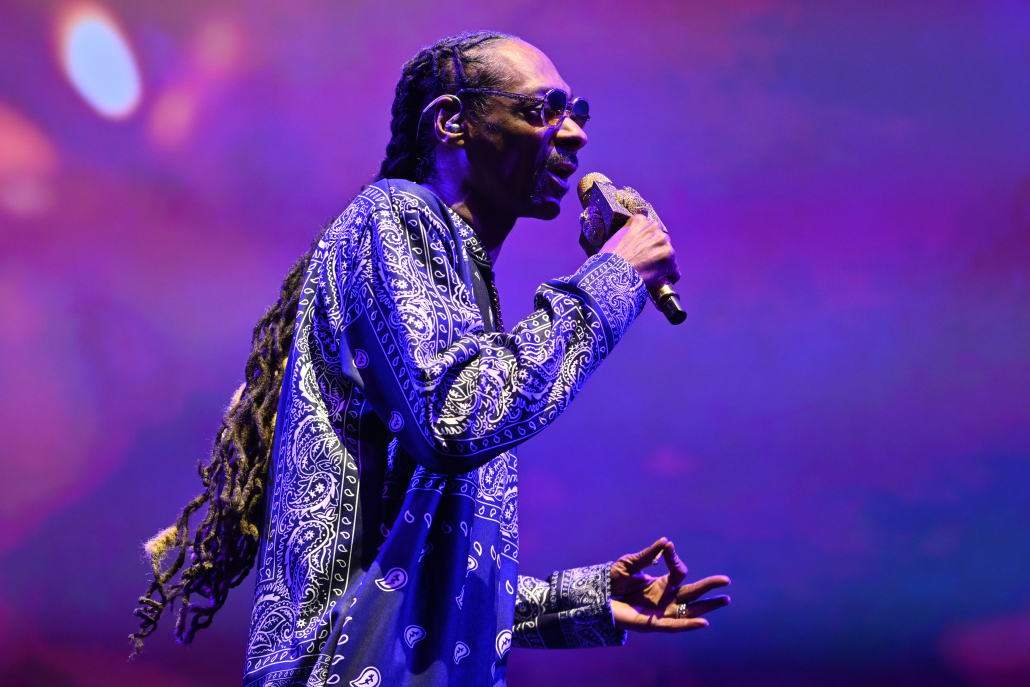 Snoop Dogg holds a microphone and a cannabis joint while performing.