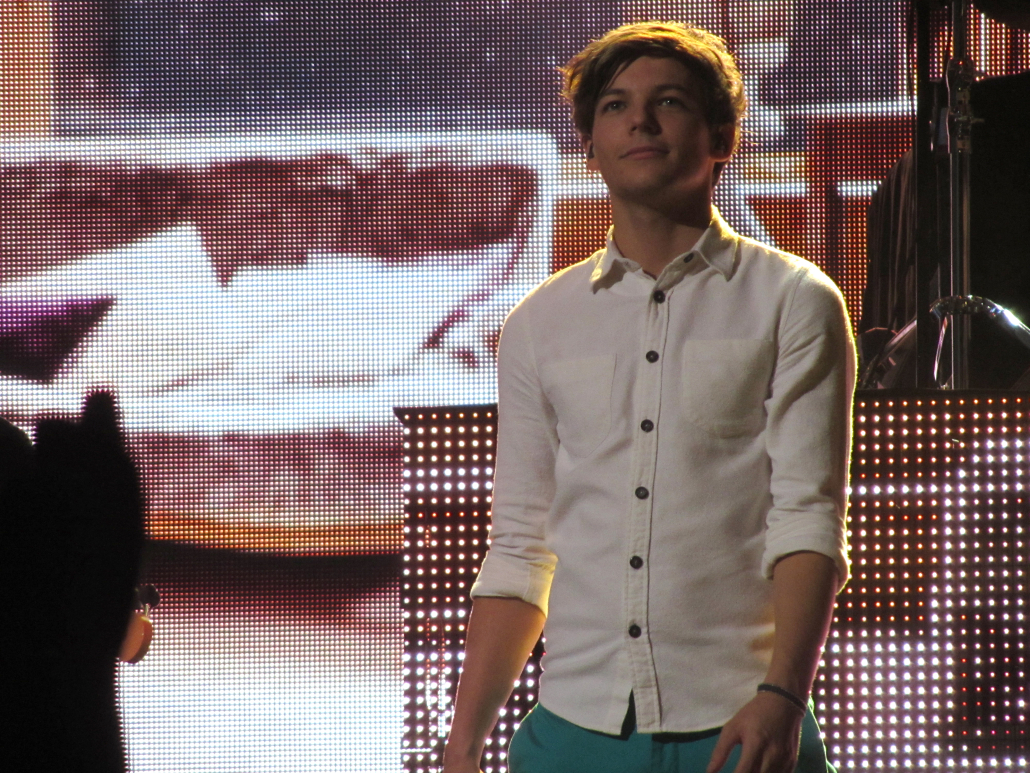 Louis Tomlinson standing on stage in white shirt.