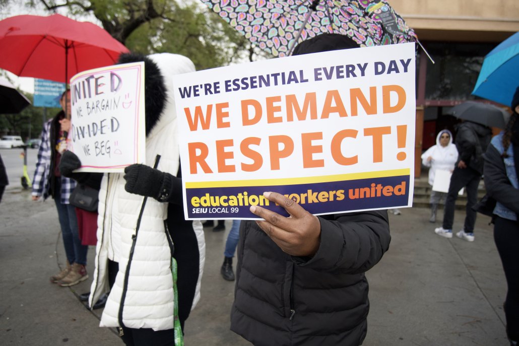 A protestor holds a sign reading "We're essential every day. We demand respect!"