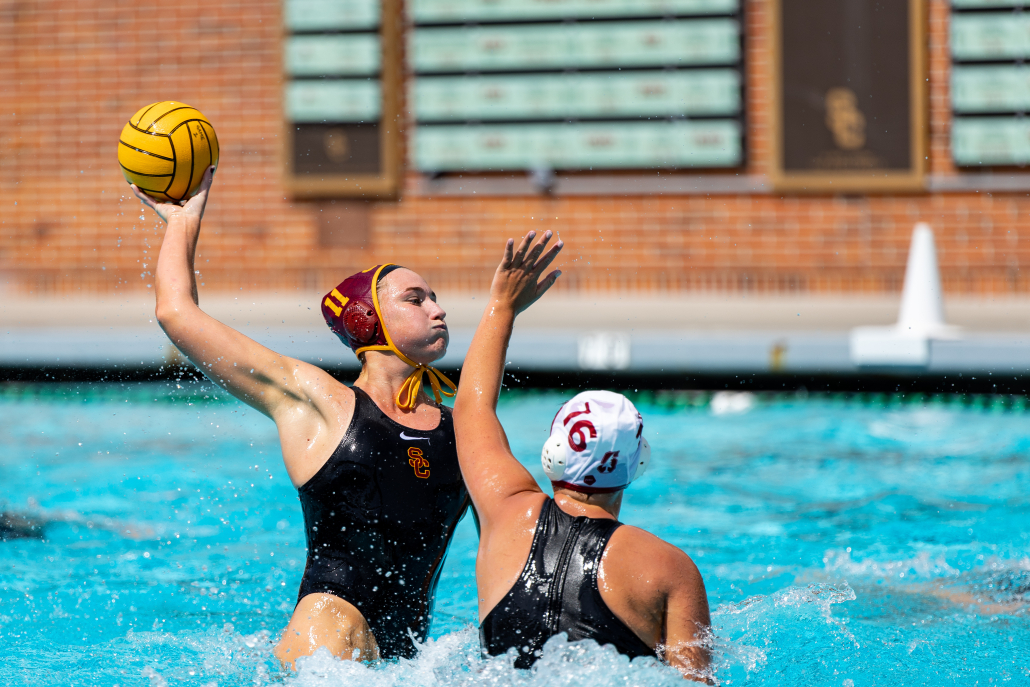 Water polo player rises above the water to get height over a Stanford player with the ball in her hand