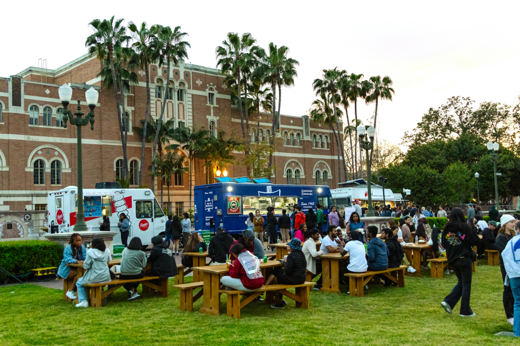 Students sit at picnic tables in front of food trucks in McCarthy Quad. 