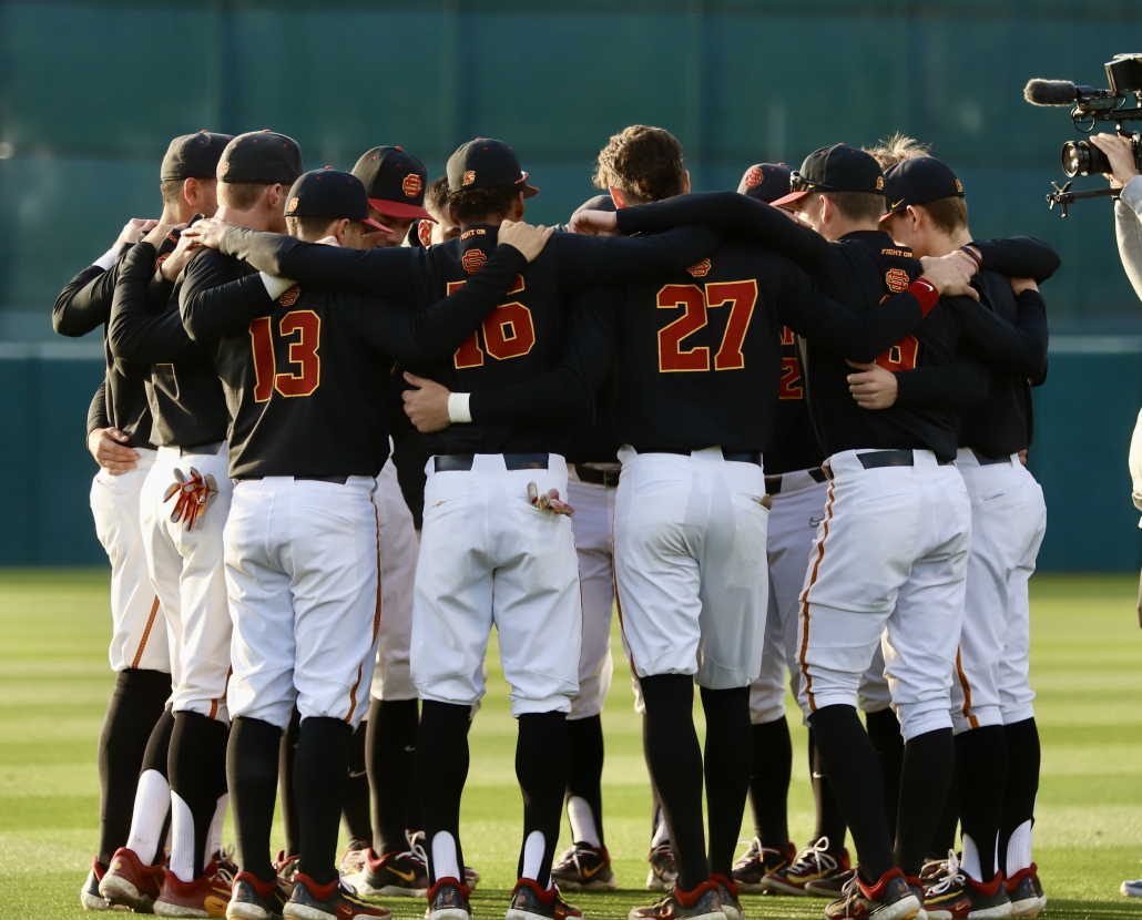 The USC baseball team wearing black uniforms gathers around each other in a huddle.