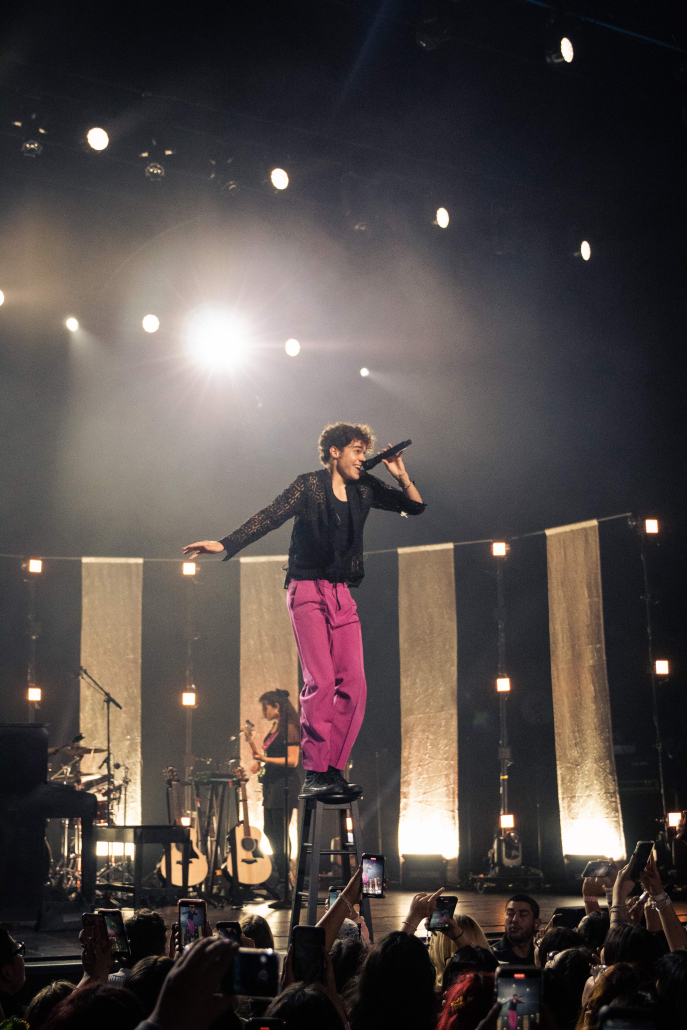 The California native multi-hyphenate stands on a stool.