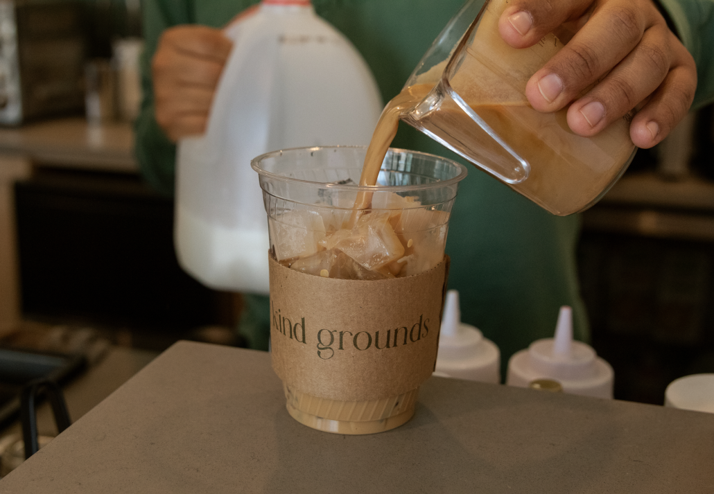 A barista pours coffee into a plastic cup with ice