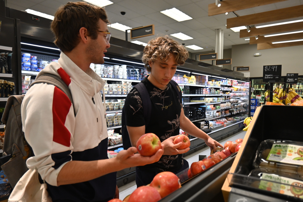 two students holding apples in a grocery store