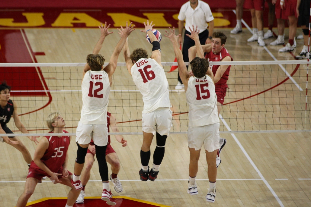 Three USC volleyball players jump up at the end to block a ball.