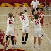 Three USC volleyball players jump up at the end to block a ball.