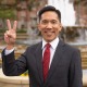Beong-Soo Kim stands in front of the ShumWay fountain in a black suit and a red tie. He holds up a v for victory.