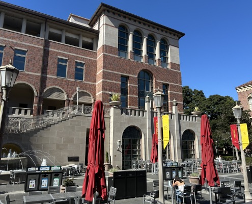 Folded red umbrellas rise above the outdoor tables at the Tutor Campus Center, while the Tutor Campus Center building is in the background.