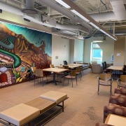 The graduate student lounge is filled with brown desks, seats and more. A large mural on one of the walls features an agrarian landscape with train tracks slicing down the middle.