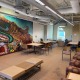 The graduate student lounge is filled with brown desks, seats and more. A large mural on one of the walls features an agrarian landscape with train tracks slicing down the middle.