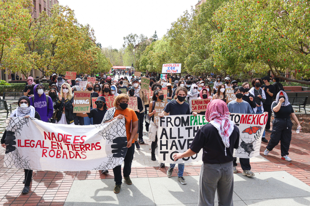 Protestors march at USC Village holding various signs. One sign reads "From Palestine to Mexico all the walls have got to go."